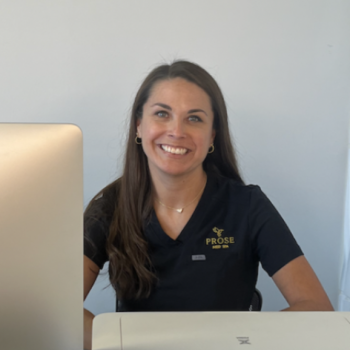 a woman sitting at a table with a laptop and smiling at the camera